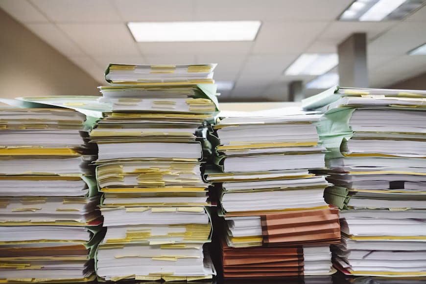 Paper files and documents stacked on an office desk.