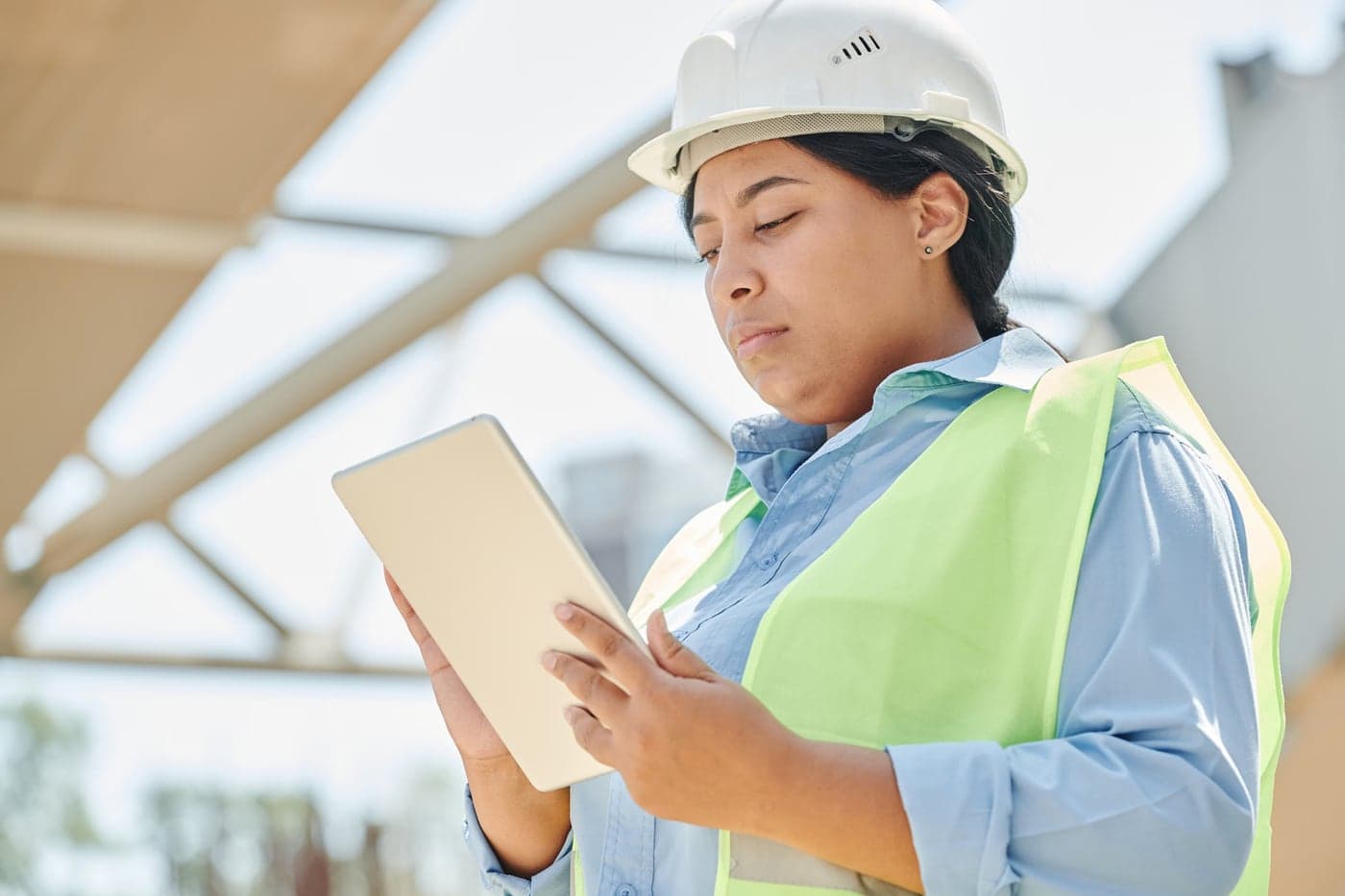 An engineer in a hard hat reviewing a tablet at a construction site.